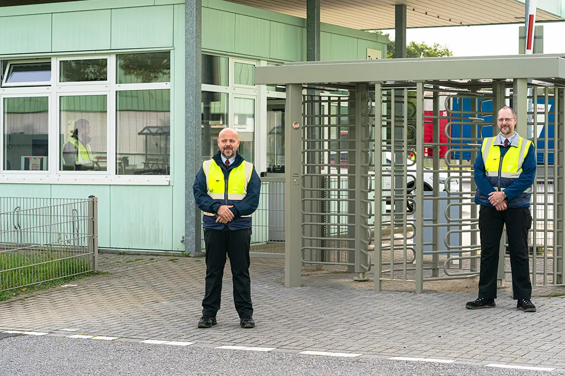 Zwei Sicherheitsbeamte stehen vor dem Eingangstor zum Werksgelände und bewachen es.